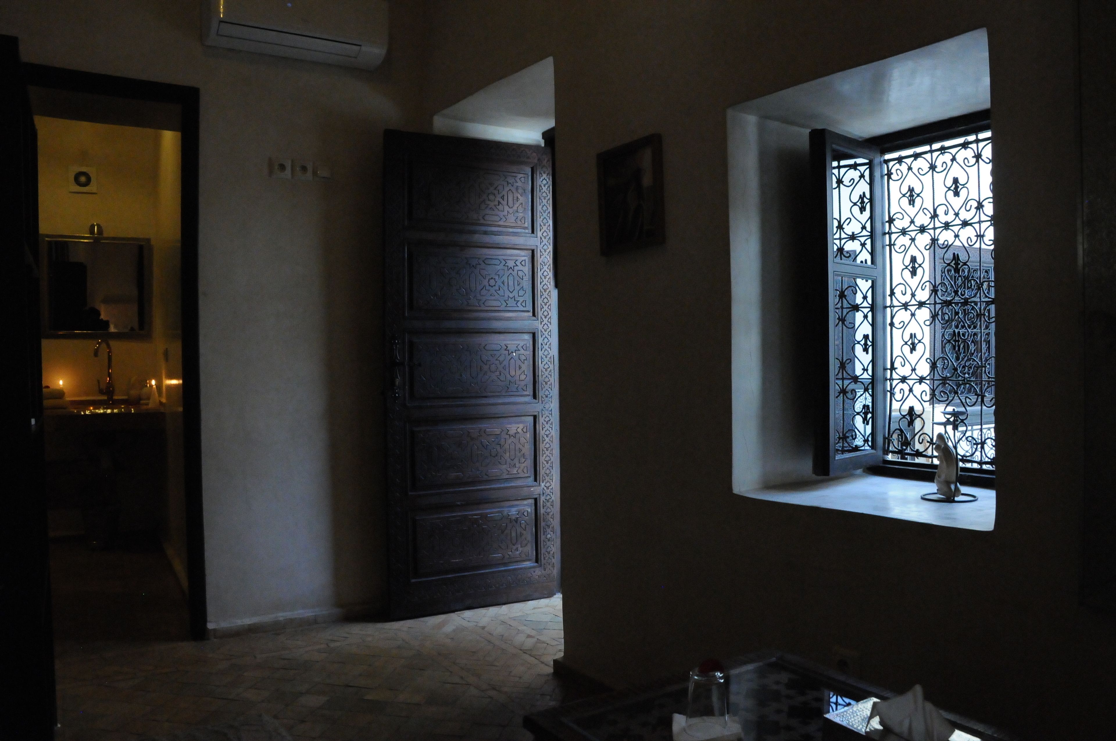 Una habitación con una puerta de madera grande, una ventana pequeña con rejas de hierro y un espejo en la pared.