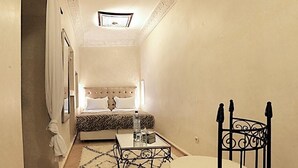 Un pasillo estrecho con una cama, una mesita y una silla metálica.