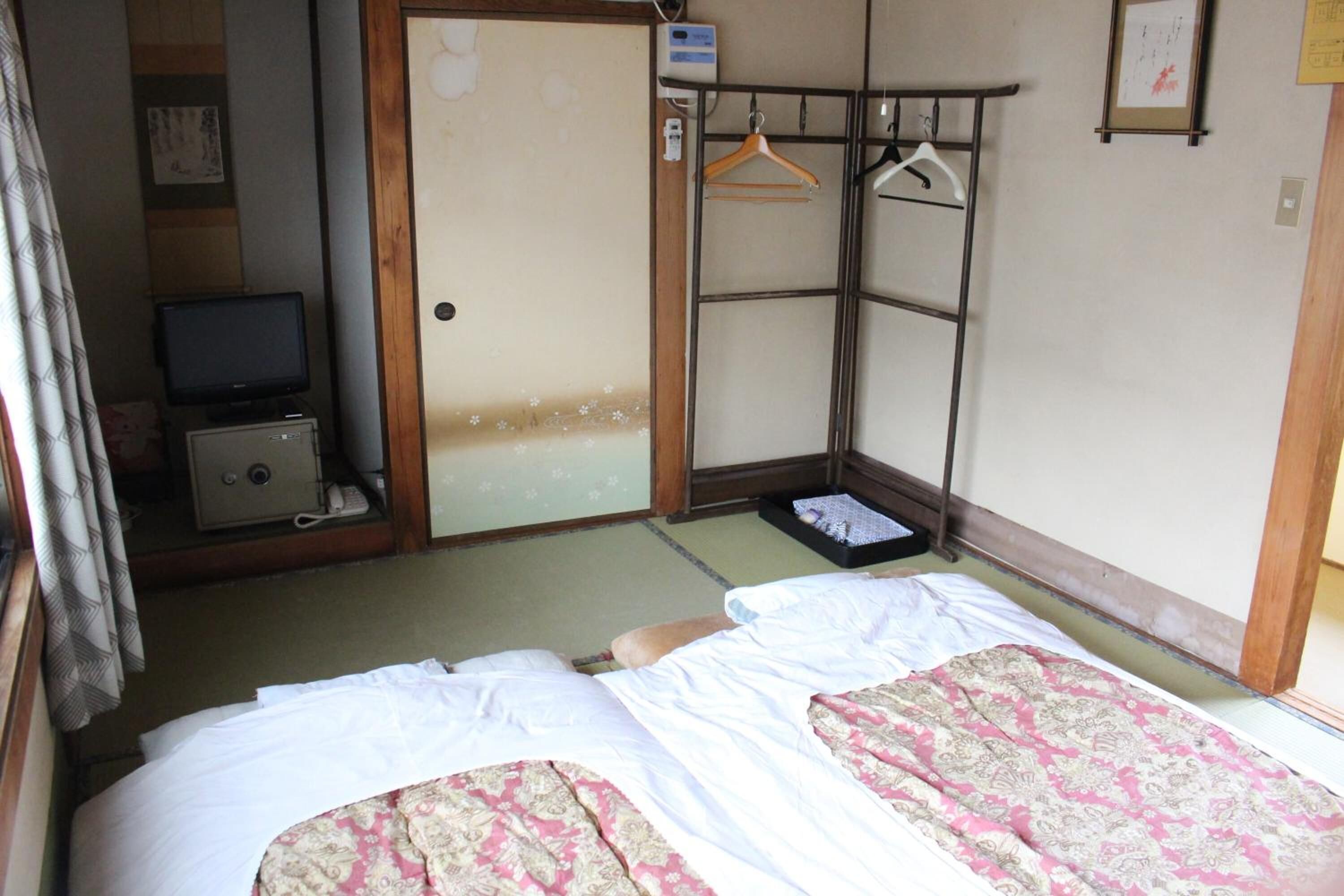 A room with two beds, a television, a wardrobe, and a hanging clothes rack.