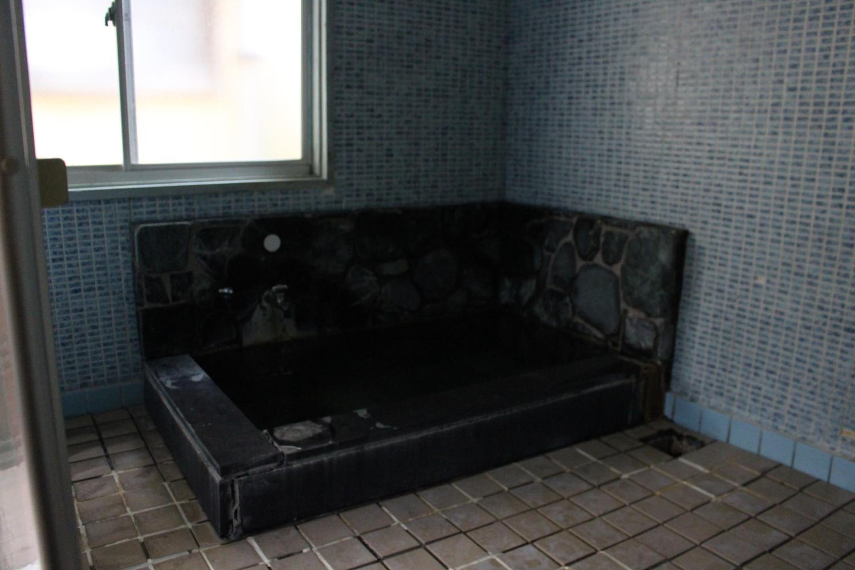 A room with a stone-tubbed hot tub, tiled walls, and a window.