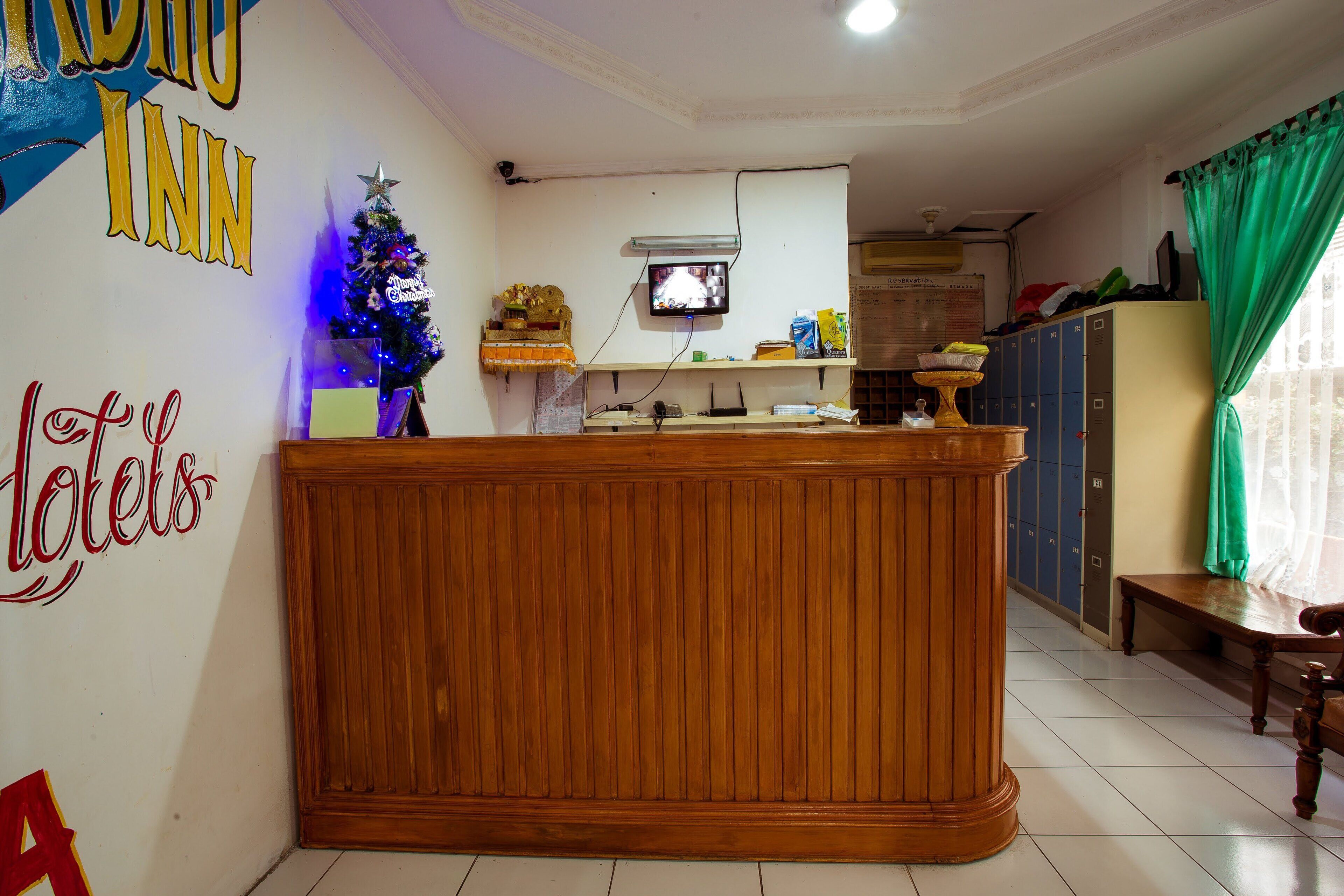 Een hotel receptie met een houten receptiebalie, een kerstboom en een aan de muur bevestigde televisie.