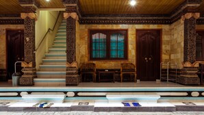 A staircase with stone columns, wooden doors, and a seating area with chairs. - Segara Sadhu Inn Kuta by ecommerceloka (Kuta)
