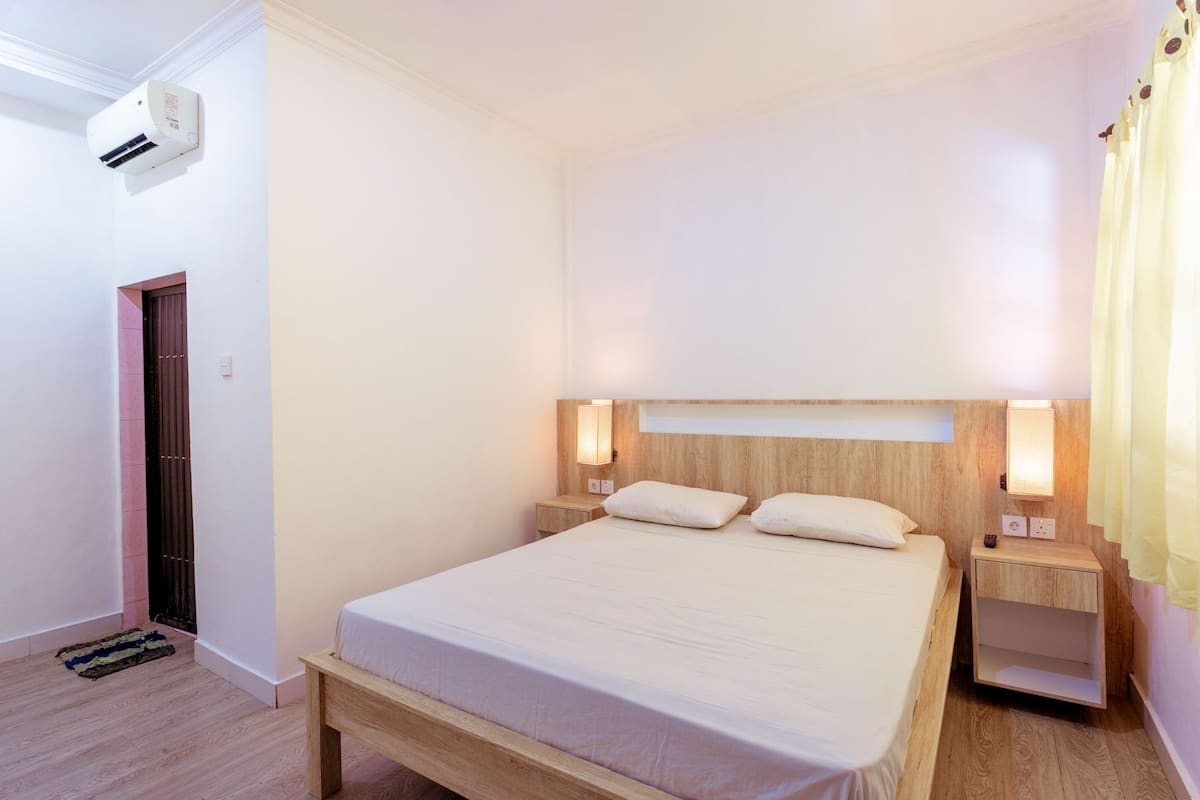 Un dormitorio con una cama de madera, mesitas de noche, aire acondicionado instalado en la pared y una puerta.