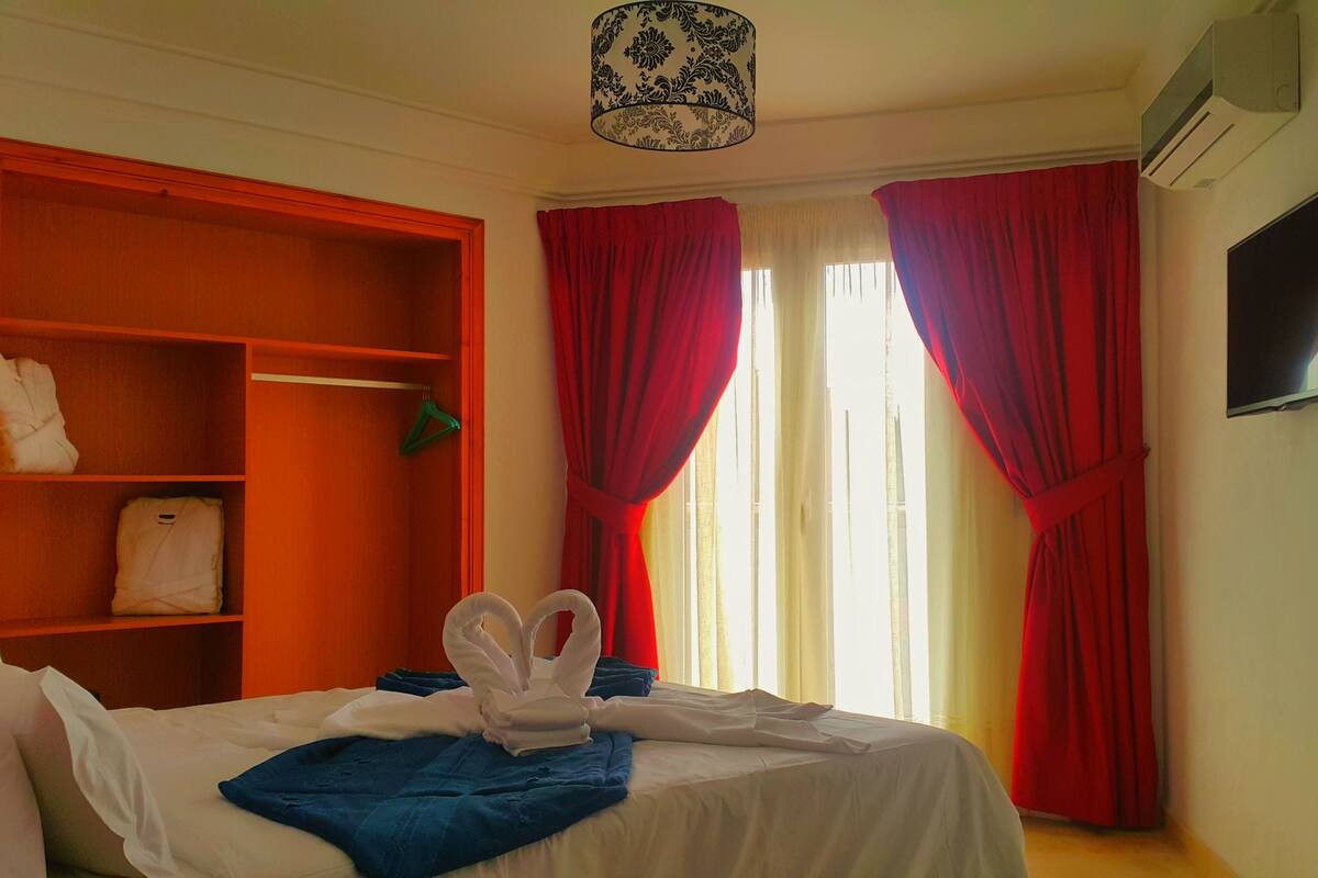 A hotel room with a bed, a wardrobe, a television, and red curtains.