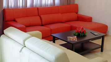 A living room with a red sofa and a white sofa. There is a coffee table with a magazine and a flower arrangement.