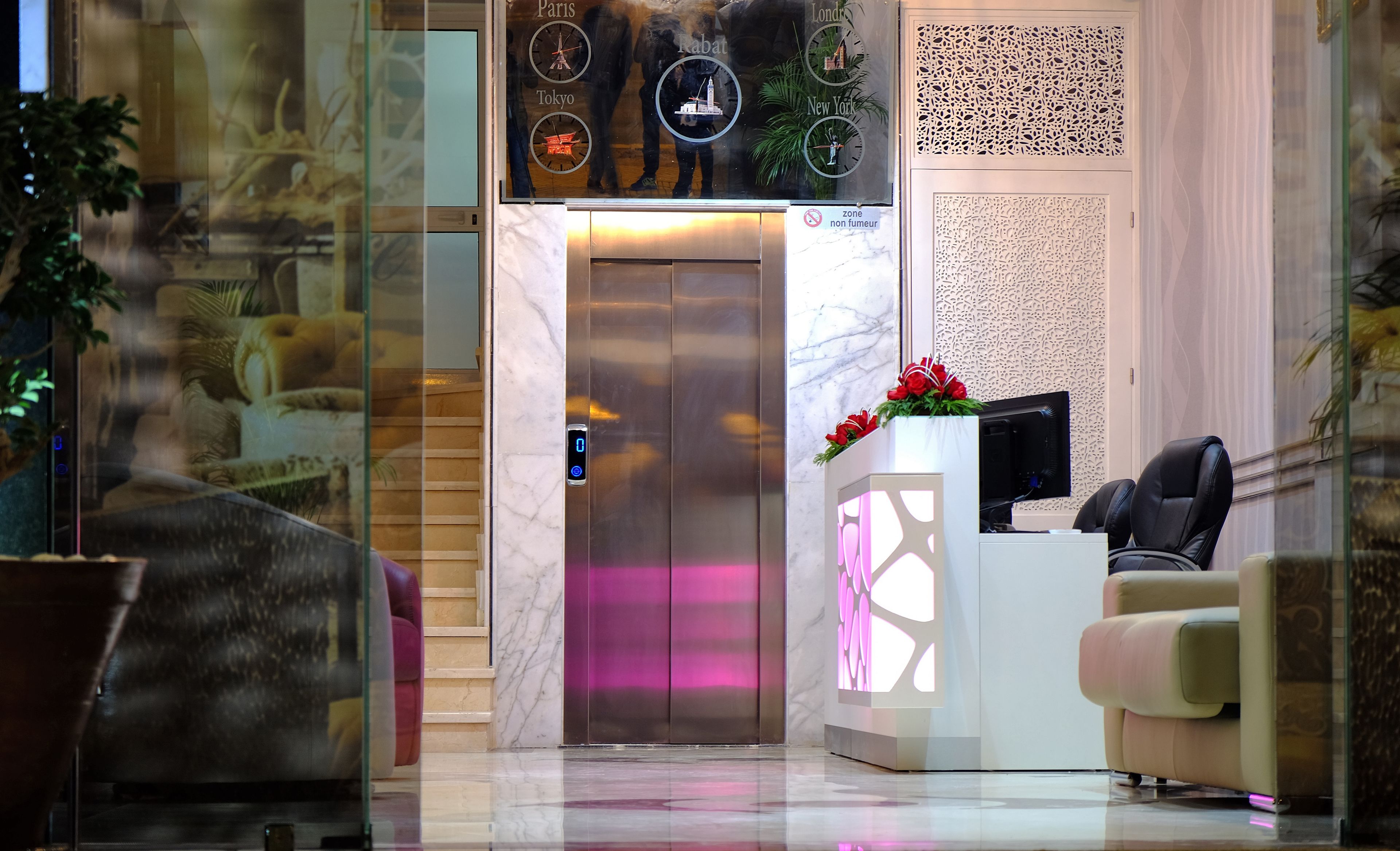 An elevator with a digital display, a reception desk with a computer, and a seating area.