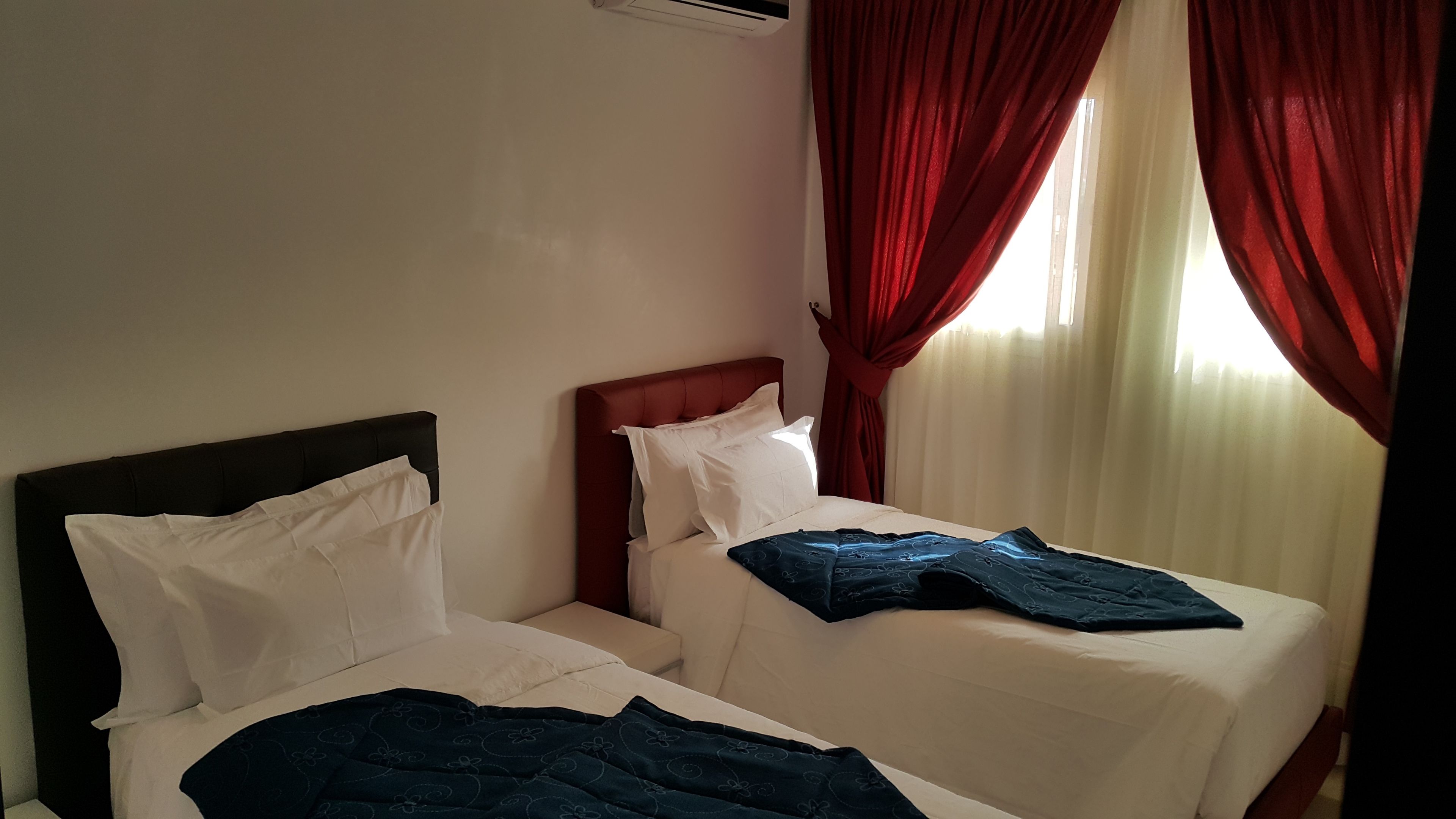 A hotel room with two beds, red curtains, and a window with sheer curtains.