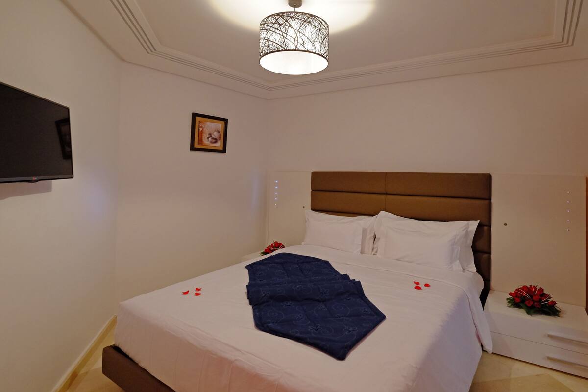 A neatly made bed with white and blue linens, a brown headboard, and a decorative blue blanket.