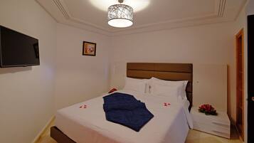 Un lit bien fait, avec du linge de lit blanc et bleu, une tête de lit marron et une couverture bleue décorative.