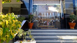 Una entrada moderna de edificio con puerta de cristal, plantas en macetas y un cartel con mensajes de bienvenida en varios idiomas.