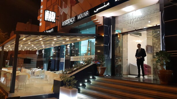 Una entrada de hotel moderna con fachada de vidrio, área de estar al aire libre y una escalera que lleva a la entrada.
