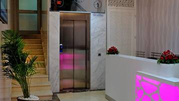 A hotel lobby with a reception desk, a staircase, and an elevator.