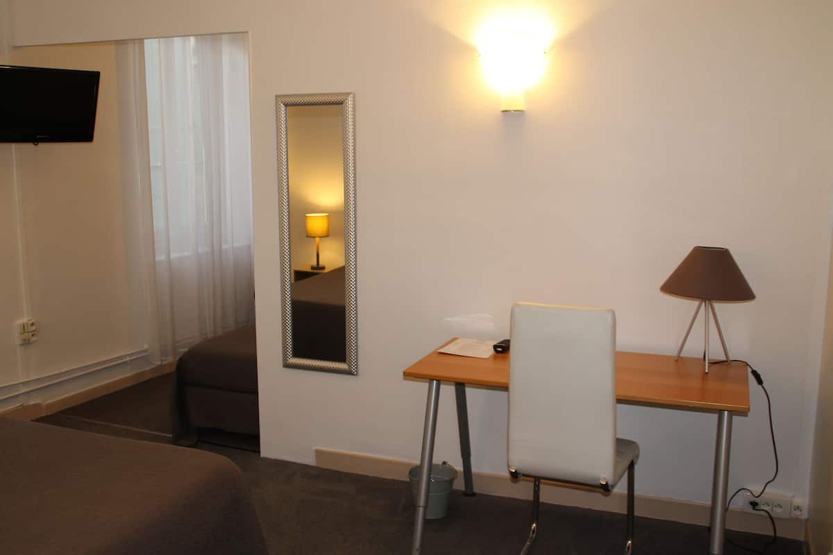 A hotel room with a bed, a desk, a chair, a lamp, a mirror, and a TV.