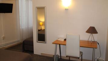 Quarto de hotel com cama, escrivaninha, cadeira, abajur, espelho e televisão.