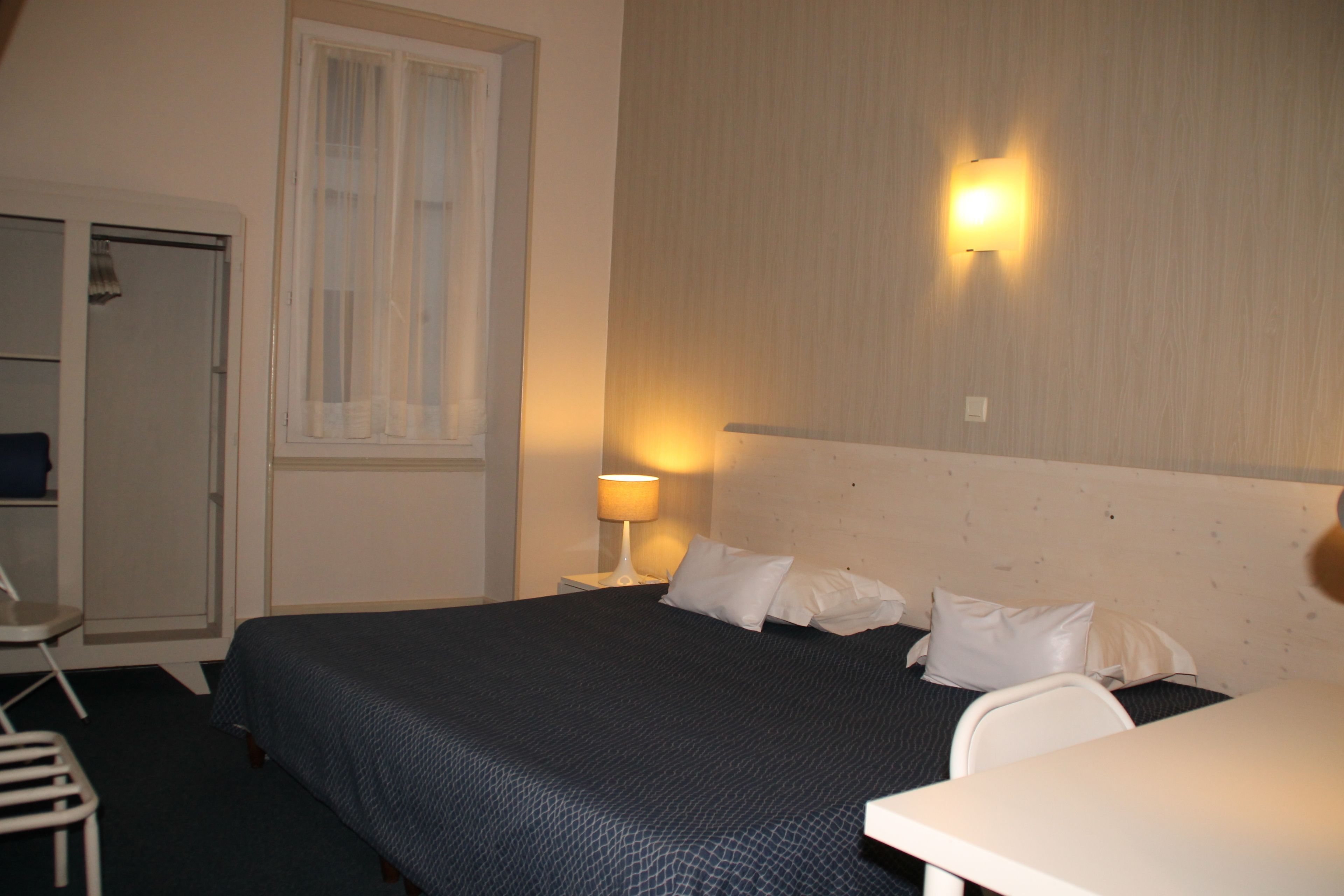 A hotel room with a bed, a desk, a chair, and a wardrobe.