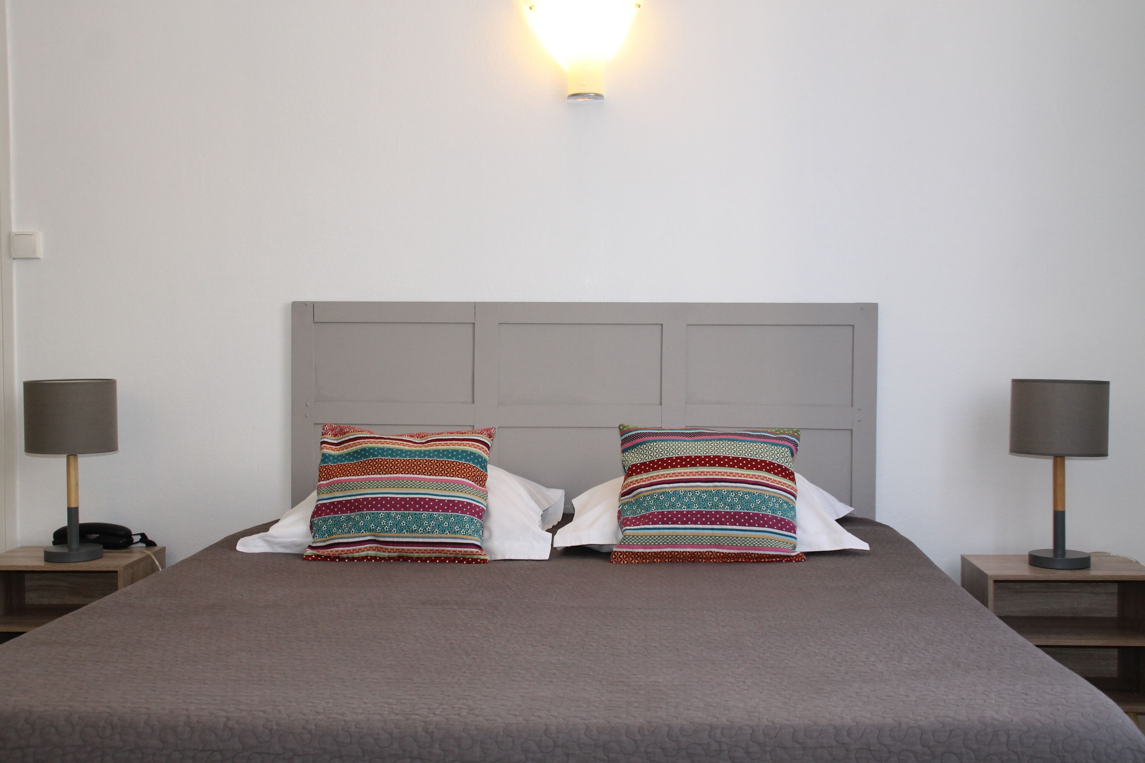 A neatly made bed with a grey headboard, two bedside lamps, and colorful striped pillows.
