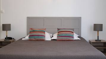 A neatly made bed with a grey headboard, two bedside lamps, and colorful striped pillows.