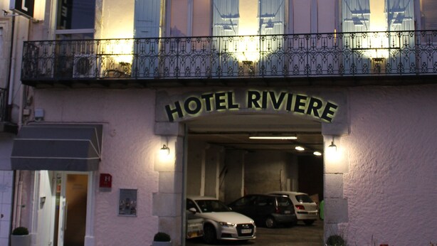 Un hotel con un letrero que dice "HOTEL RIVIERE" y un coche estacionado en la entrada.