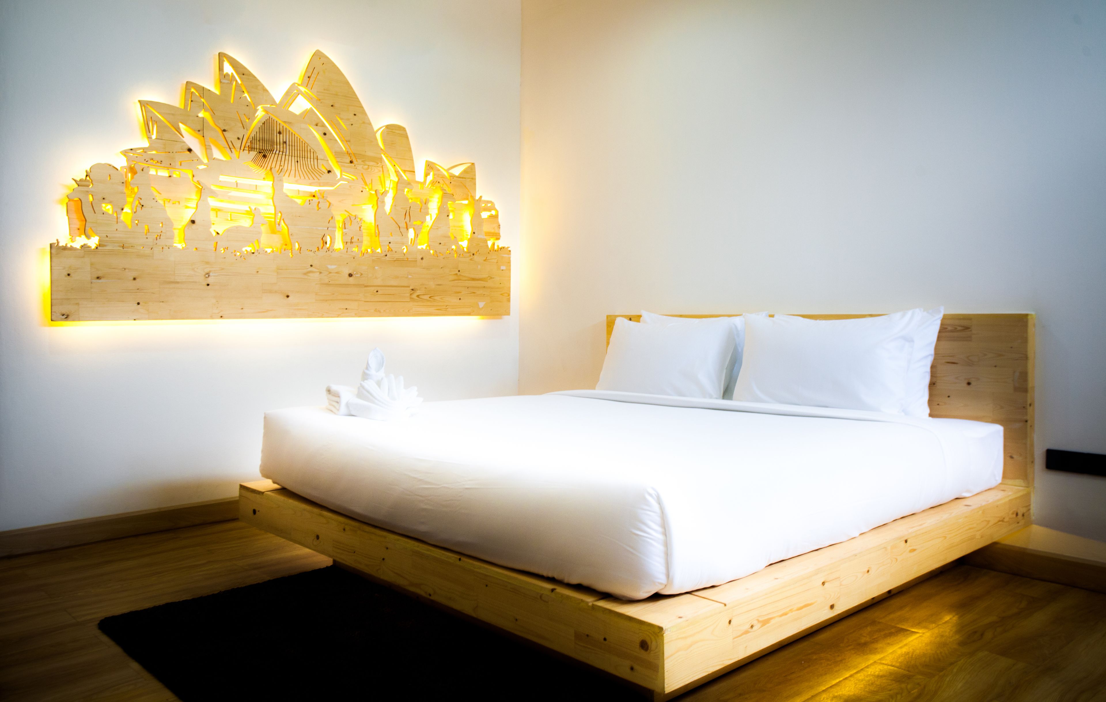 A modern bedroom with a wooden bed frame, white bedding, and a unique illuminated wall art piece.
