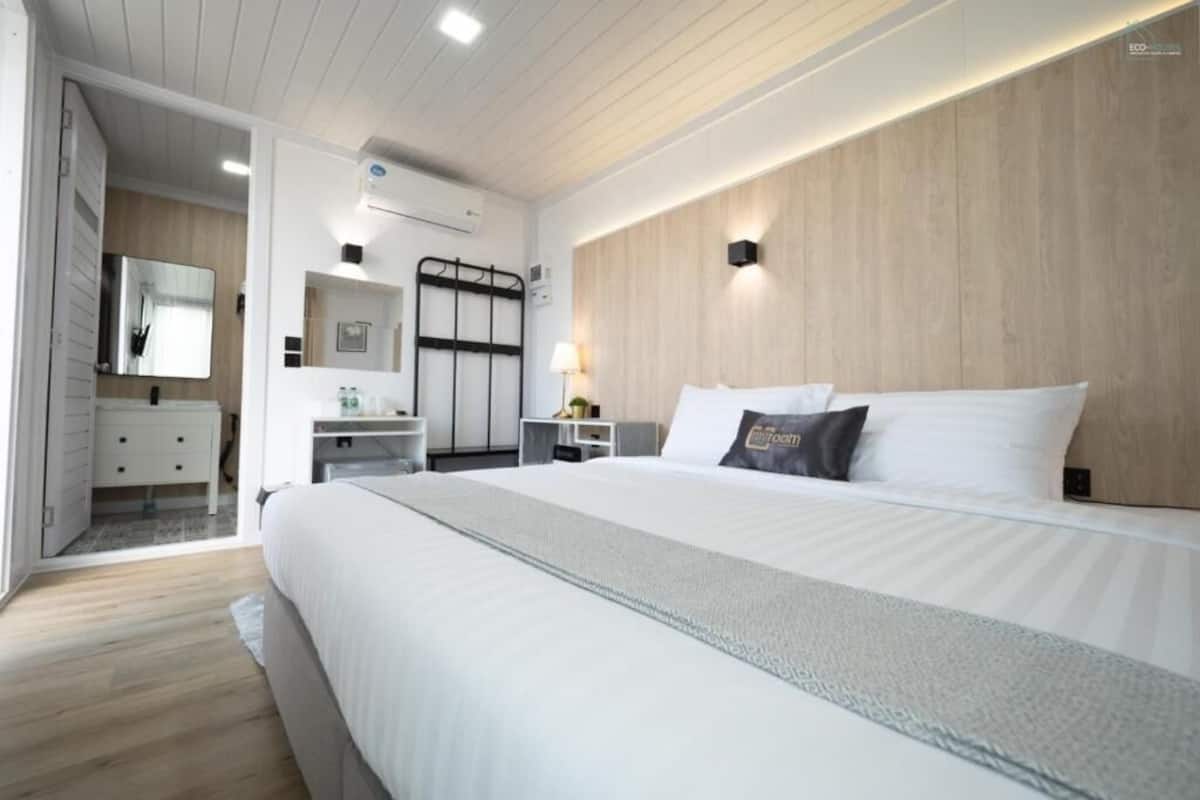 A modern hotel room with a large bed, a bedside table, a mirror, and a wooden accent wall.