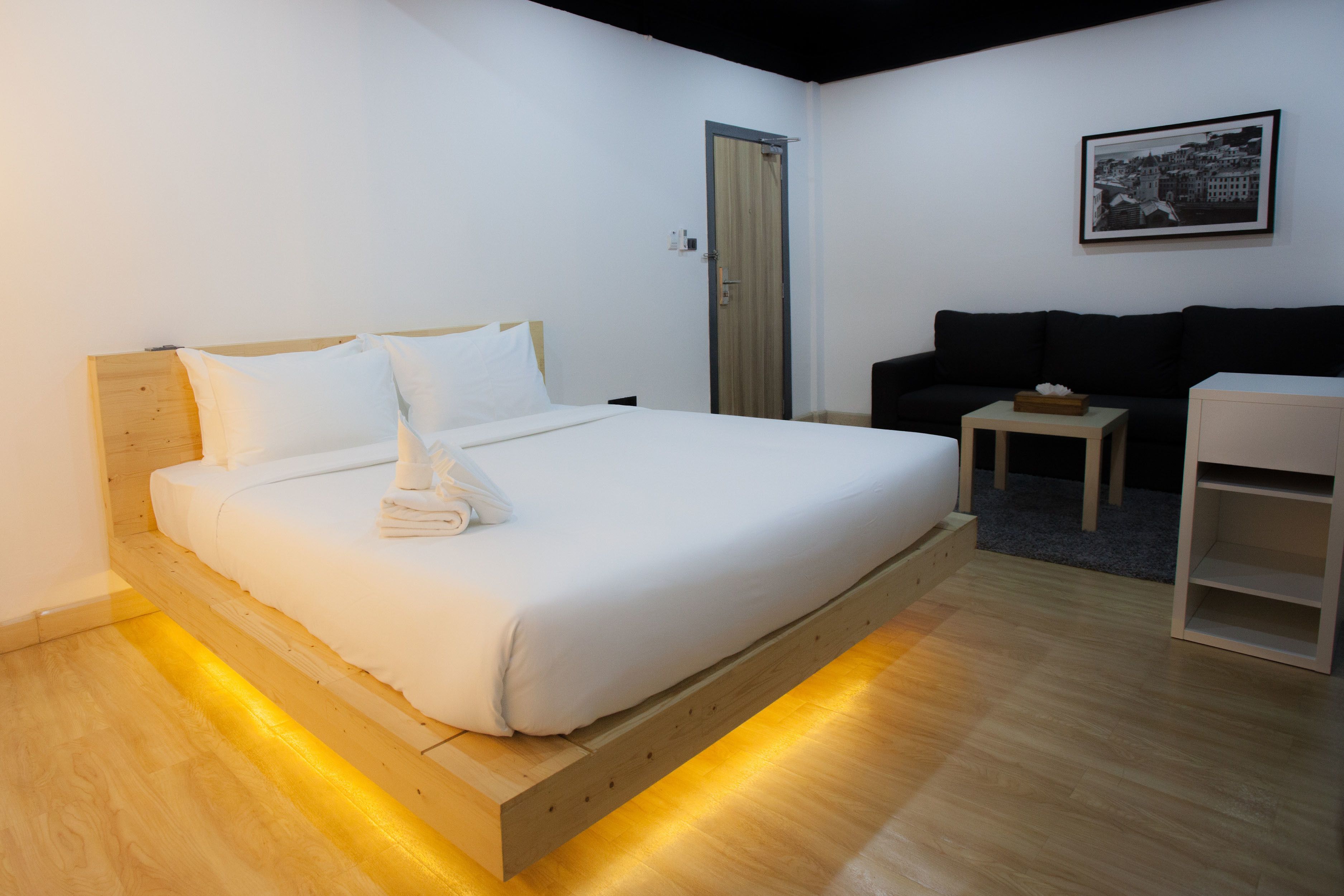 Une chambre d’hôtel moderne avec un lit en bois, une petite table, un canapé et un tableau encadré au mur.