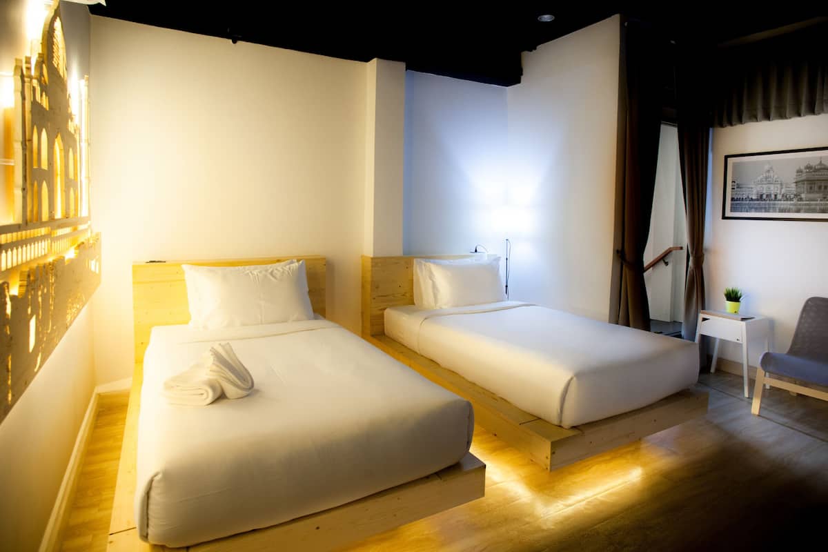 A hotel room with two single beds, a small table with a chair, and a framed picture on the wall.