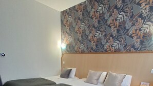 Habitación de hotel con dos camas, un papel tapiz estampado y suelo de madera.