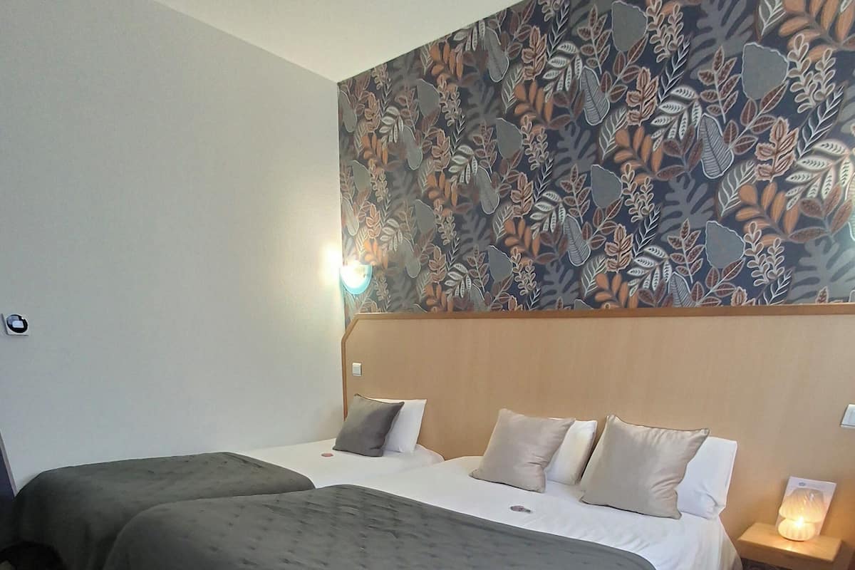 Une chambre d’hôtel avec deux lits, un mur décoré de motifs et un plancher en bois.