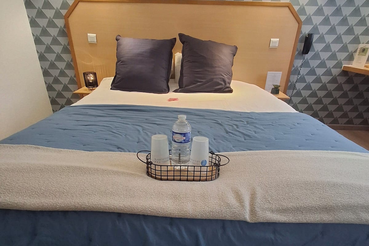 Une chambre d’hôtel avec un lit, deux lampes de chevet, une table de chevet, un plateau avec des articles de toilette et un mur à motifs.