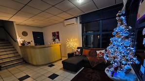 Un vestíbulo de hotel con mostrador de recepción, una escalera, un ventanal grande y un árbol de Navidad.