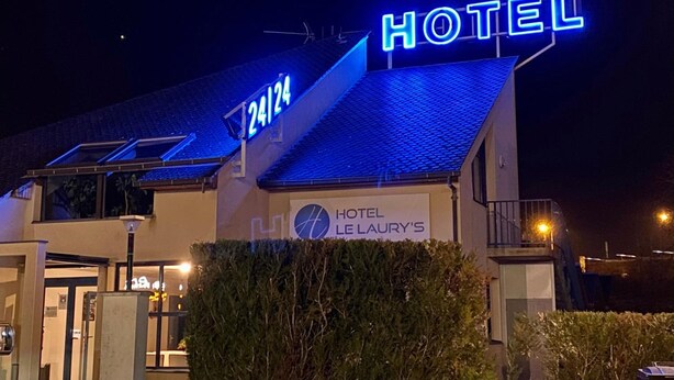 Un hotel con un letrero de neón que indica servicio las 24 horas y el nombre "Hotel LeLaurys".