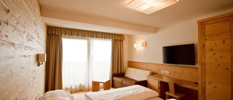 A hotel room with two beds, a TV, a wooden wardrobe, and a window with curtains.