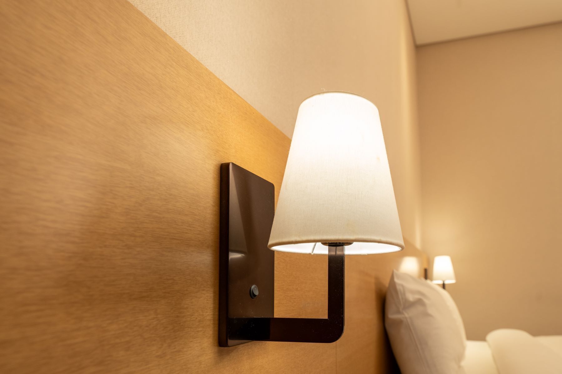 Una lámpara de pared con pantalla blanca en una habitación de hotel.