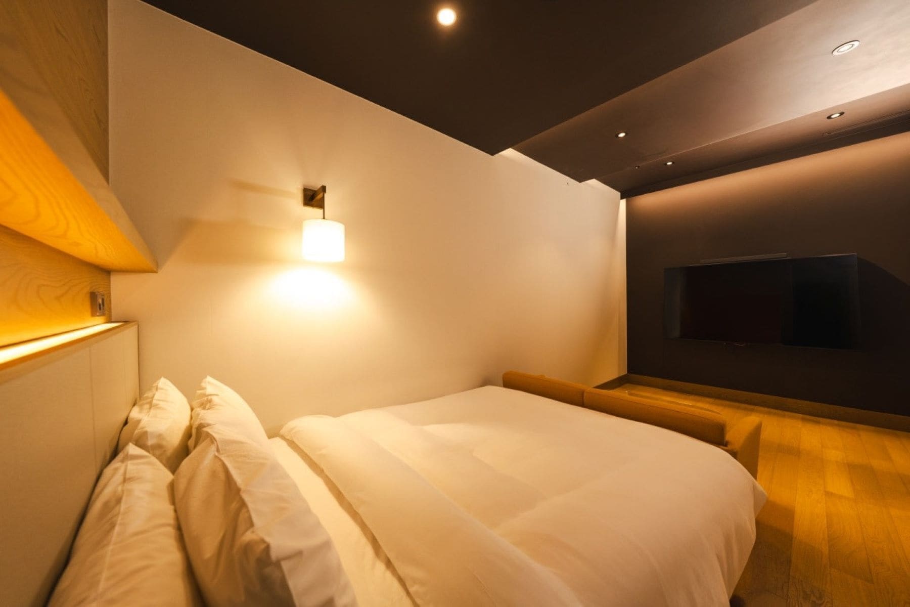 A modern bedroom with a bed, a wall-mounted TV, and recessed lighting.