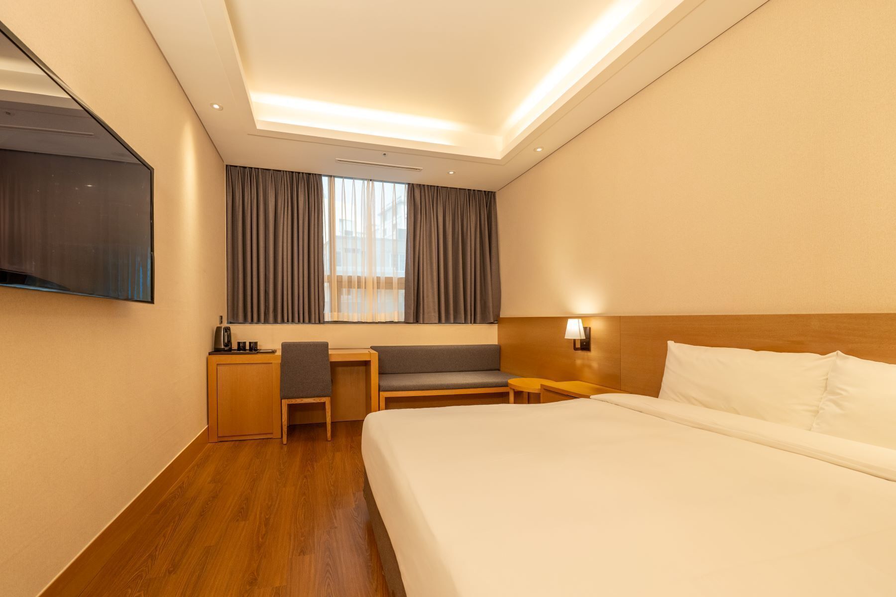A hotel room with a bed, a desk, a chair, a TV, and a window with curtains.