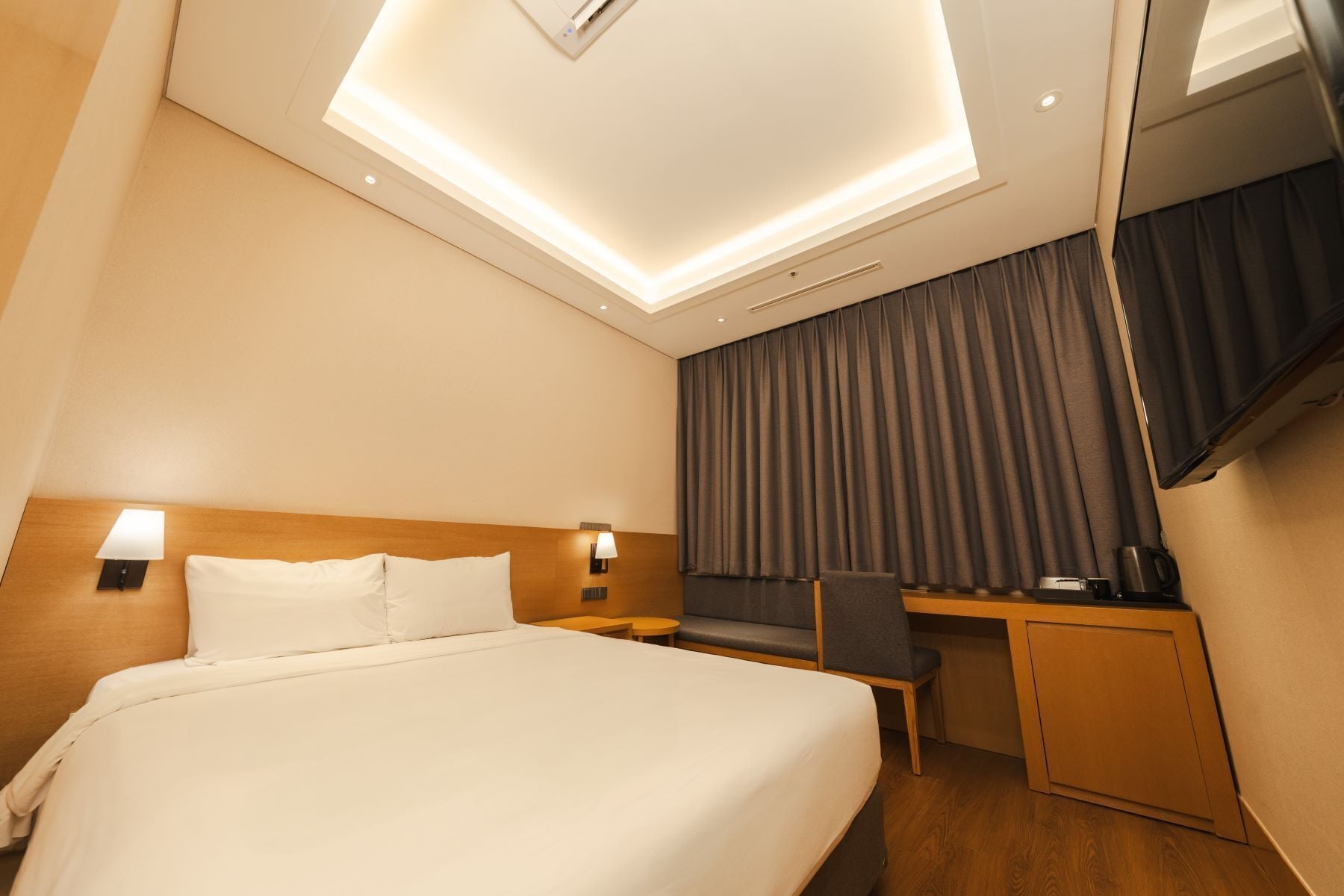 A hotel room with a large bed, a desk, a chair, a TV, and a coffee machine.