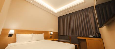 A hotel room with a large bed, a desk, a chair, a TV, and a coffee machine.