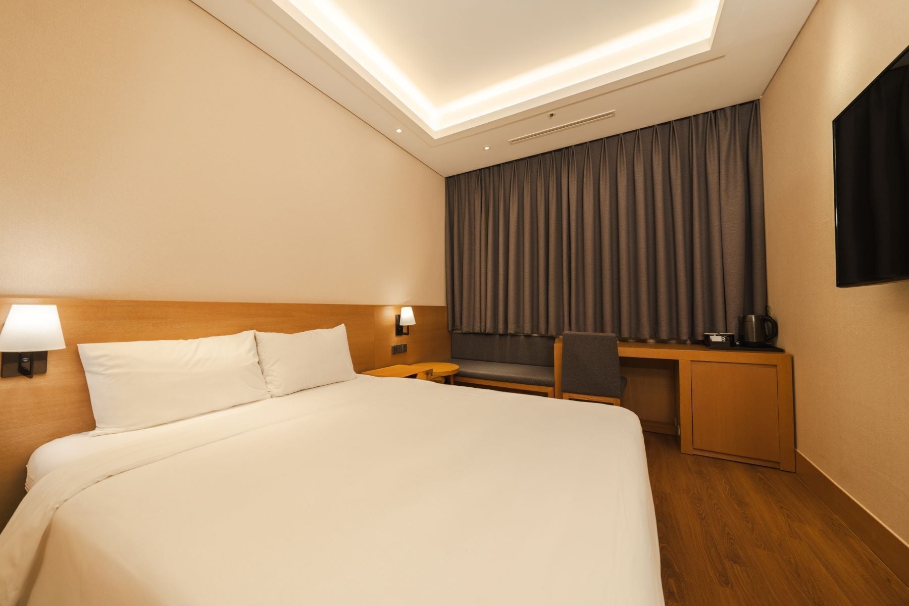 A hotel room with a large bed, a desk with a chair, a TV, and a window with curtains.
