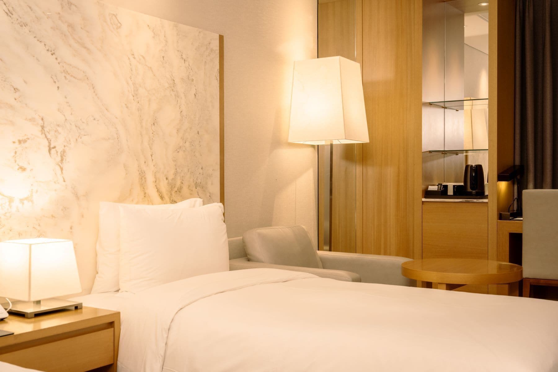 A hotel room with a bed, a nightstand, a lamp, a sofa, a small round table, and a mirror.