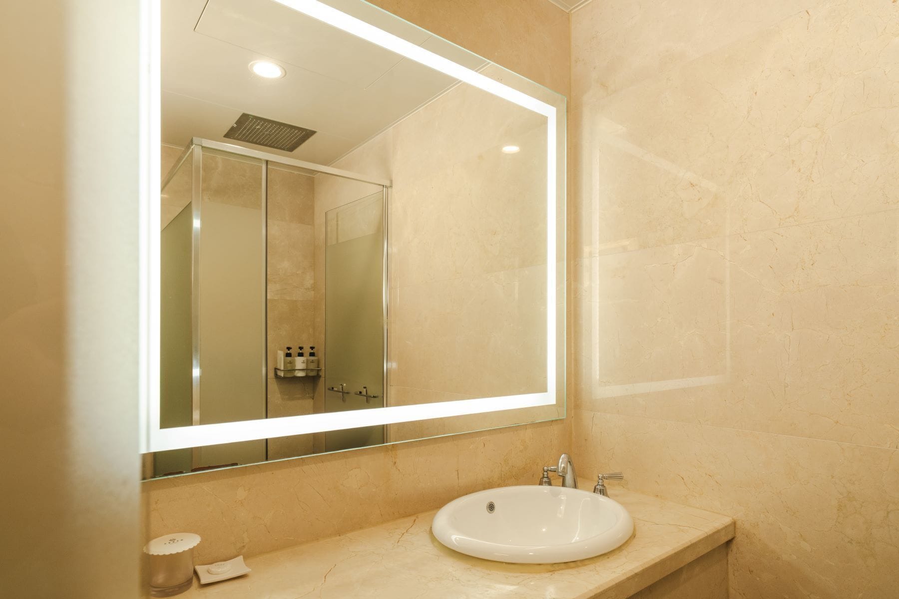 A bathroom with a large mirror, a sink, and a shower.