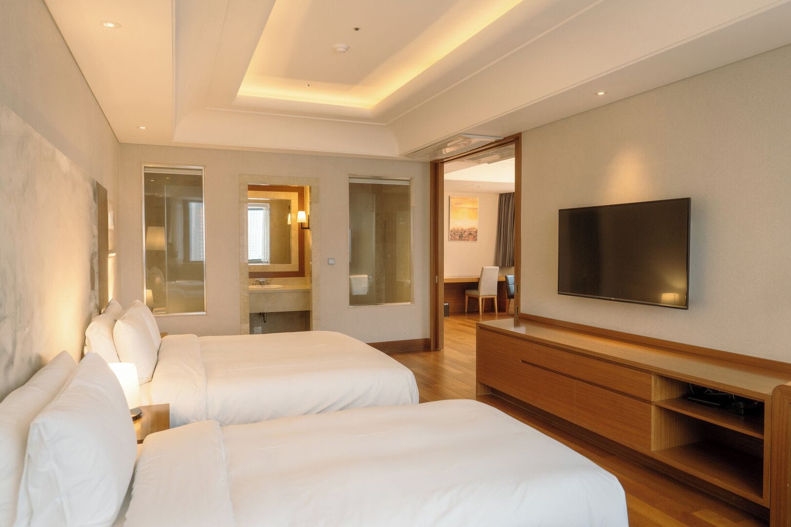 A hotel room with two beds, a TV, a desk, and a bathroom visible through an open door.