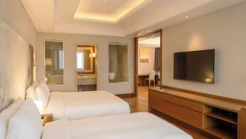 A hotel room with two beds, a TV, a desk, and a bathroom visible through an open door.