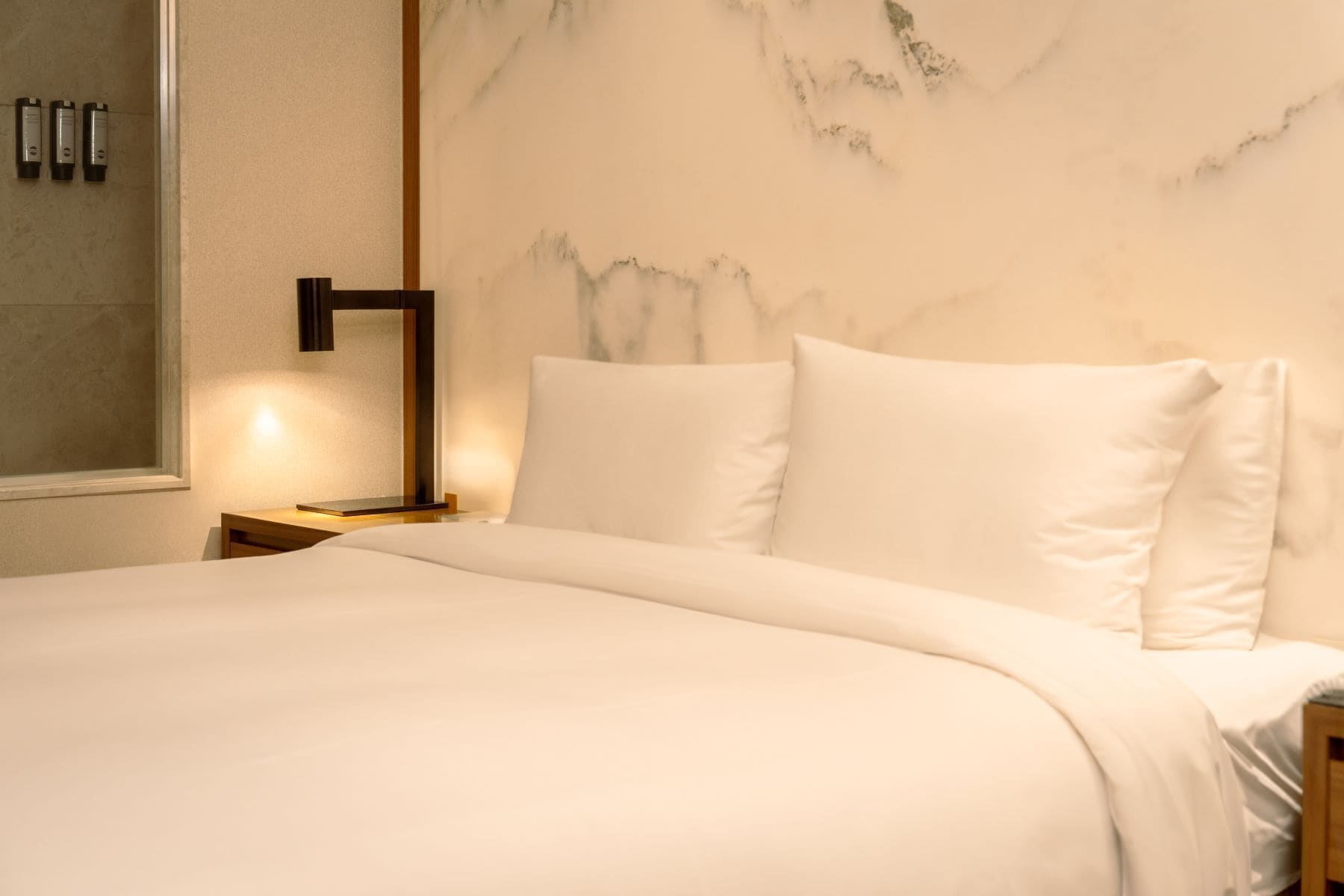 Un lit bien fait, avec du linge de lit blanc, dans une chambre d’hôtel.