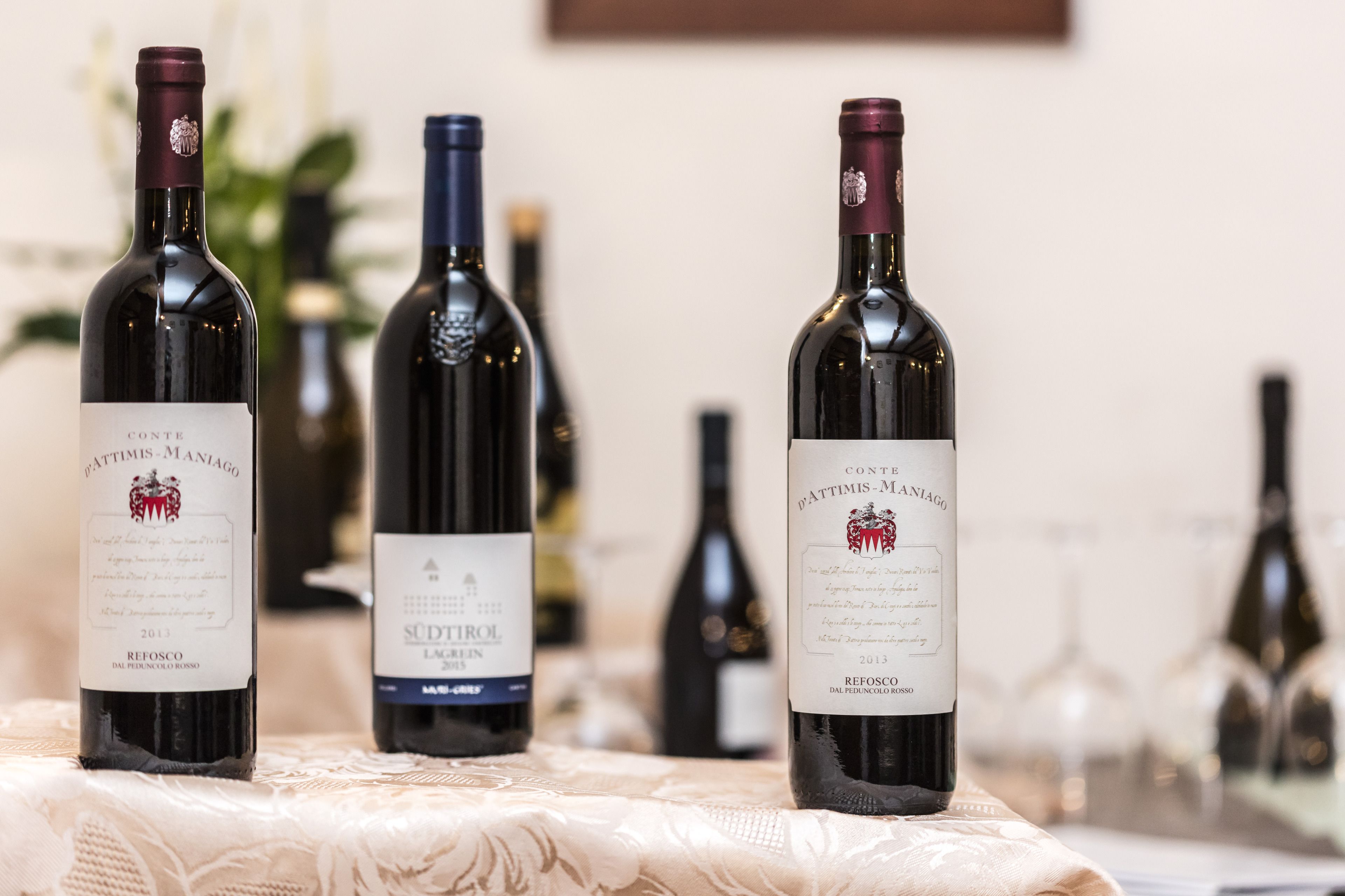 Three wine bottles on a table with a lace tablecloth.
