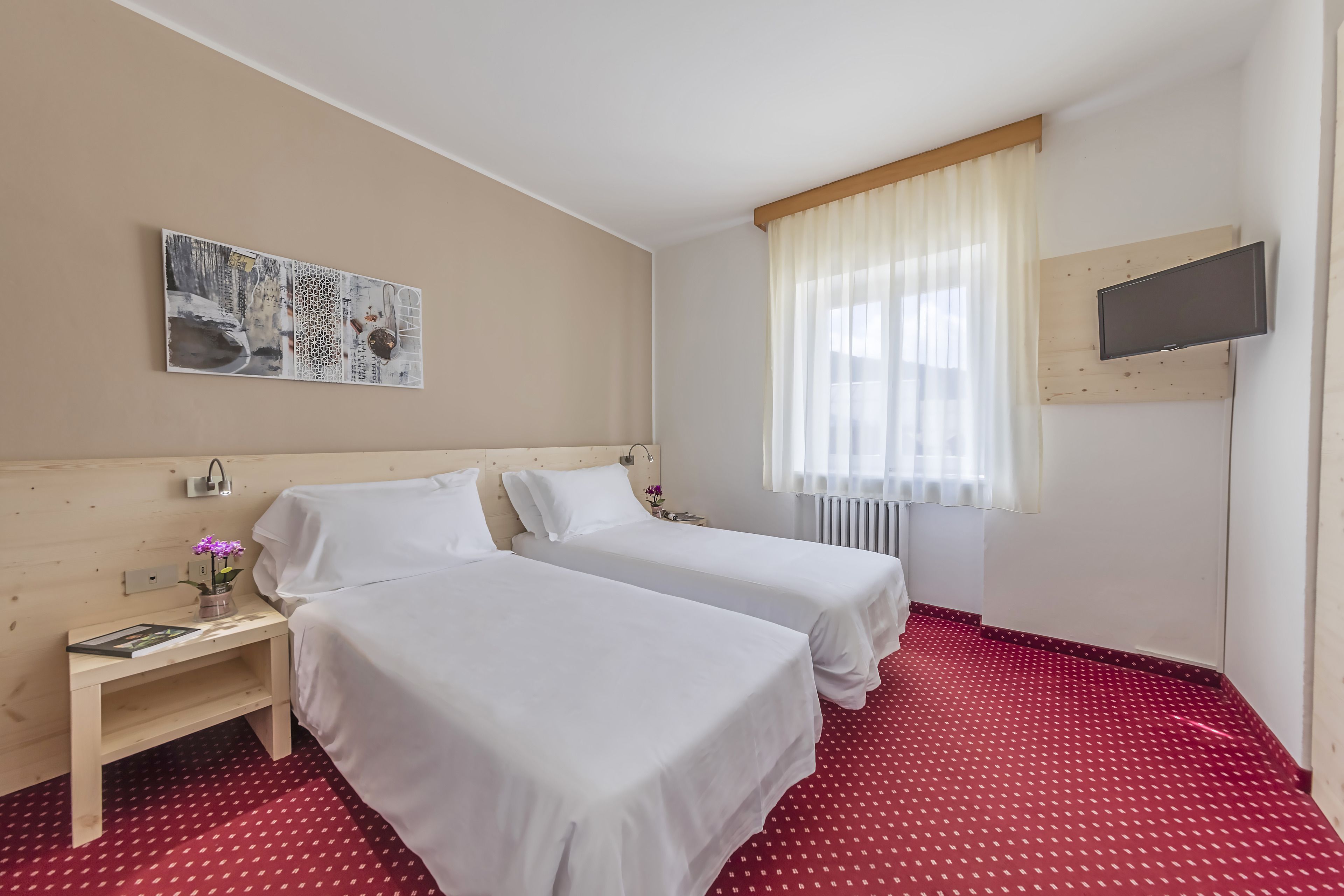 Habitación de hotel con dos camas, un televisor en la pared, un cuadro y una ventana con cortinas.