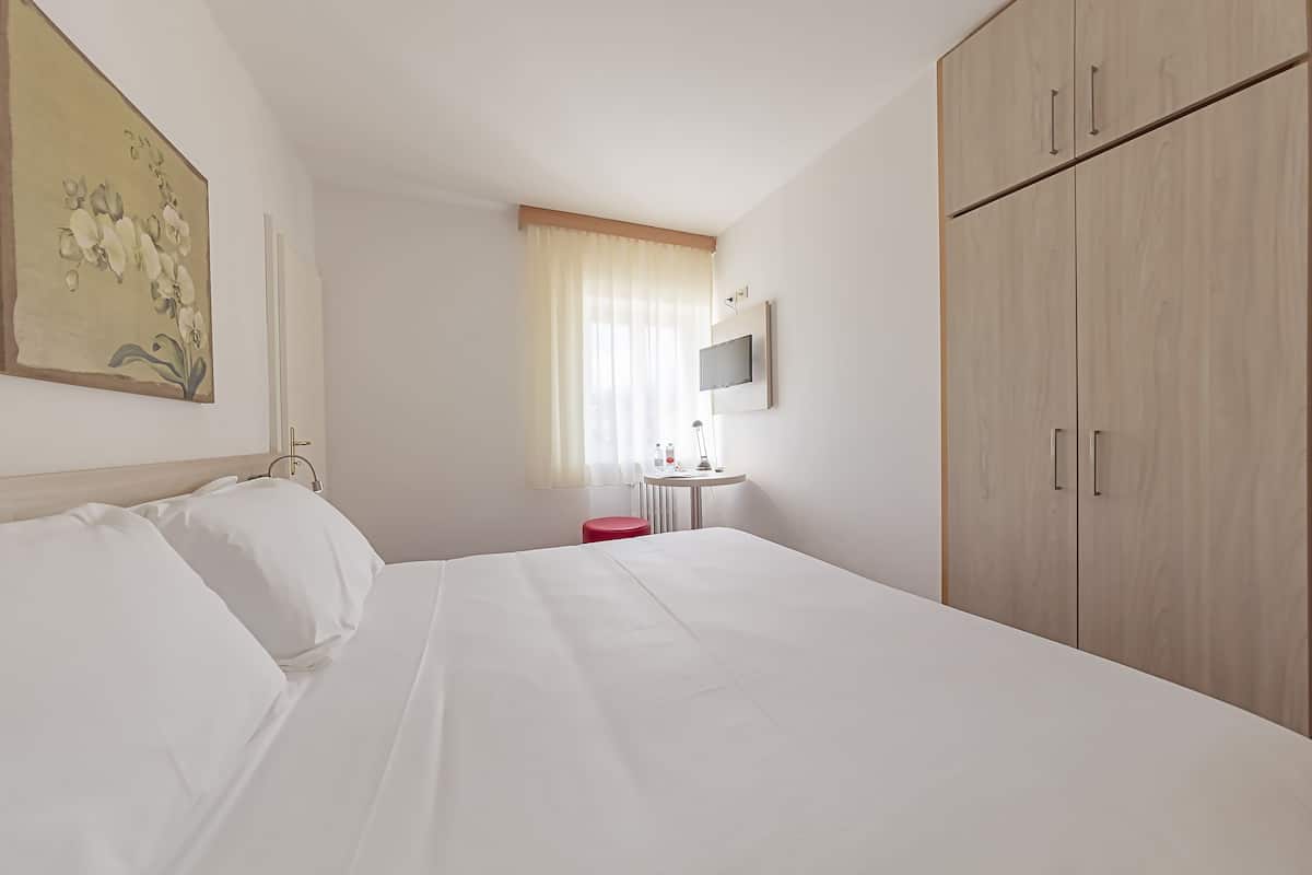 A hotel room with a bed, a desk, a TV, and a wardrobe.
