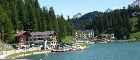 Un hotel a orillas del lago con varias edificaciones, un muelle con barcos y montañas al fondo.
