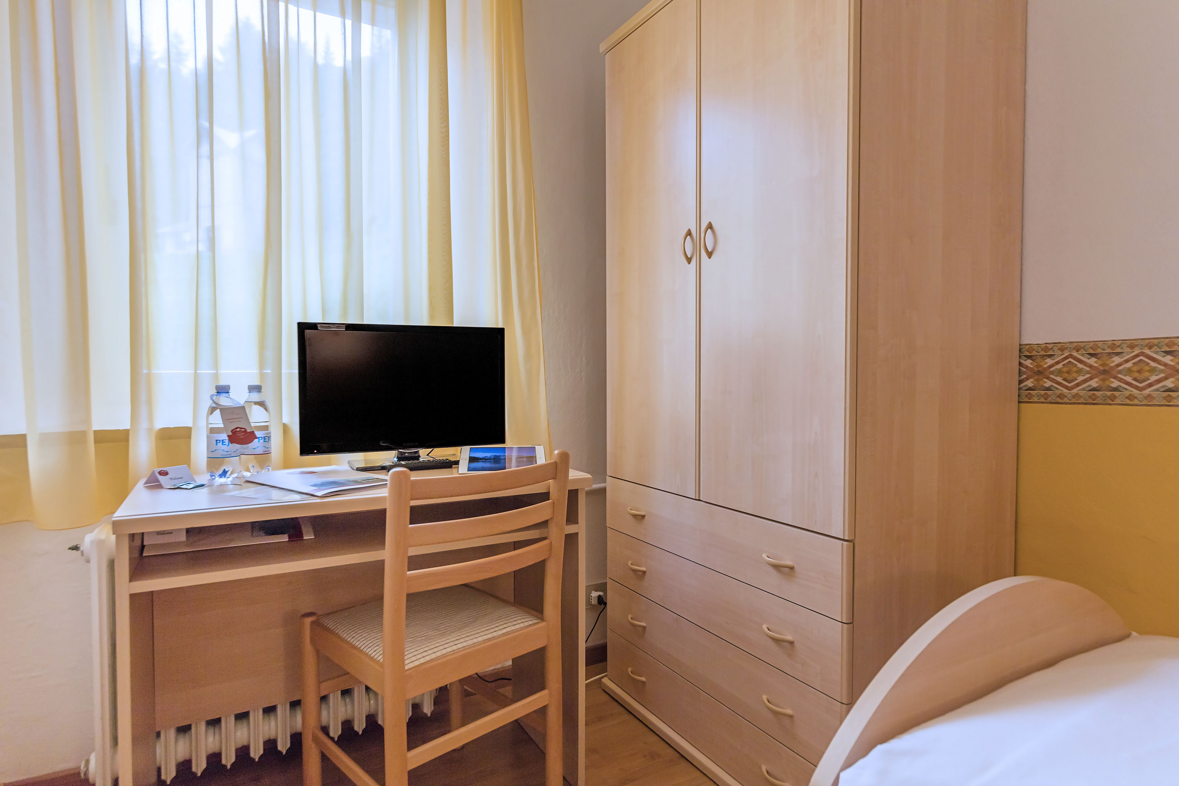Huoneessa on puinen työpöytä, tietokone, tuoli, vaatekaappi ja sänky.