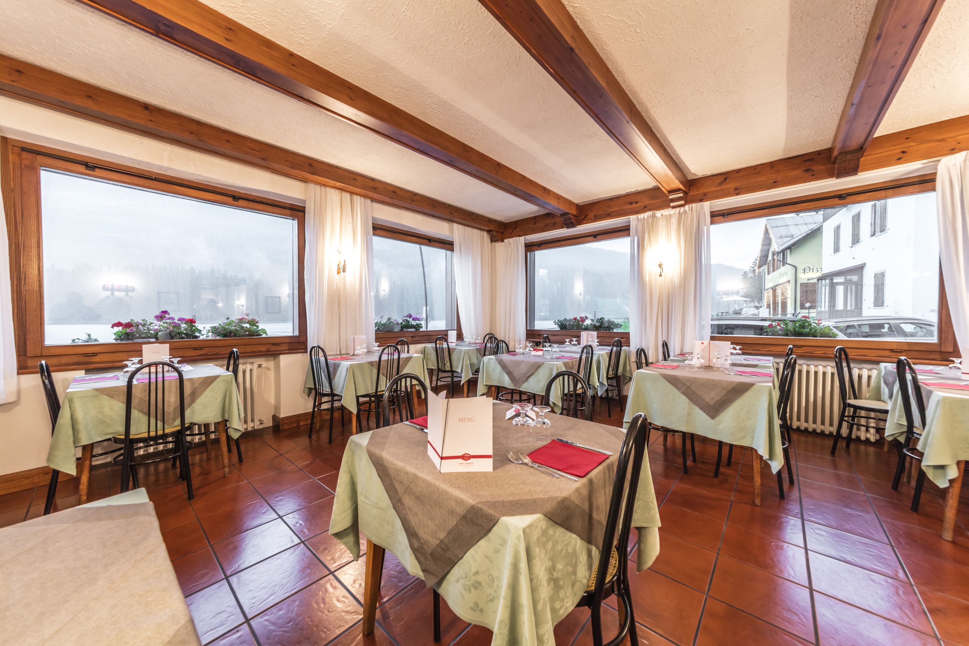 Un restaurante con varias mesas, sillas y grandes ventanales con cortinas.