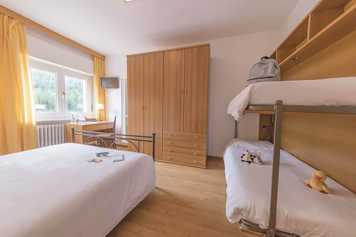 A hotel room with two beds, a wooden wardrobe, a desk with a chair, and a window with curtains.